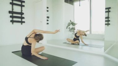 Genç bir kadın işe ara verirken stresten kurtulmak için spor salonunda yoga egzersizleri yapıyor. Aydınlık bir odada Mat 'in üstünde antrenman yapmak.