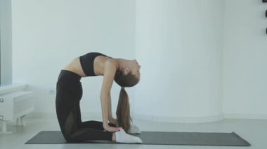 Ayakta yoga yaparken bacaklarını esneten genç bir kadın spor ya da aktif yaşam tarzının bir parçası olarak esneme hareketleri yapıyor. Sporcu kız antrenmandan önce ısınır..