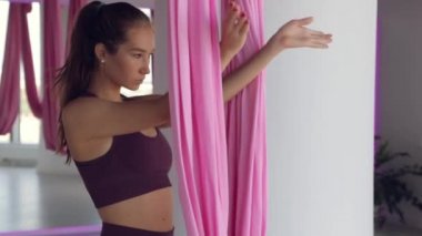 Genç bir atletik kız hamakta yoga yapıyor, sağlık egzersizleri yapıyor. Spor salonunda panoramik pencerelerle çalışma.