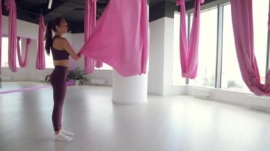 Genç bir atletik kız hamakta yoga yapıyor, sağlık egzersizleri yapıyor. Spor salonunda panoramik pencerelerle çalışma.