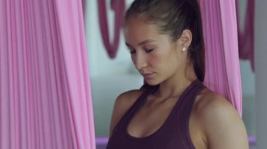 Genç bir atletik kız hamakta yoga yapıyor, sağlık egzersizleri yapıyor. Spor salonunda panoramik pencerelerle çalışma.