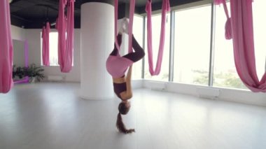 Genç bir atletik kız hamakta yoga yapıyor, sağlık egzersizleri yapıyor. Spor salonunda panoramik pencerelerle çalışma.