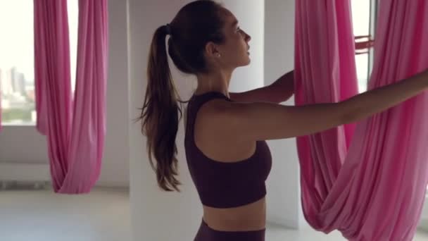 Een jong atletisch meisje doet yoga op een hangmat, oefeningen voor de gezondheid. Trainen in de fitnessruimte met panoramische ramen. — Stockvideo