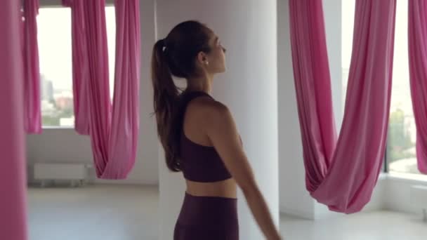 Een jong atletisch meisje doet yoga op een hangmat, oefeningen voor de gezondheid. Trainen in de fitnessruimte met panoramische ramen. — Stockvideo