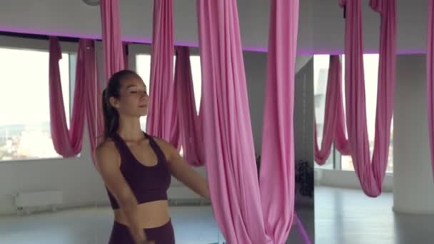 Młoda wysportowana dziewczyna ćwiczy jogę na hamaku, ćwiczy dla zdrowia. Trening w siłowni z panoramicznymi oknami. — Wideo stockowe
