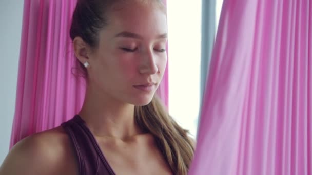 Een jong atletisch meisje doet yoga op een hangmat, oefeningen voor de gezondheid. Trainen in de fitnessruimte met panoramische ramen. — Stockvideo