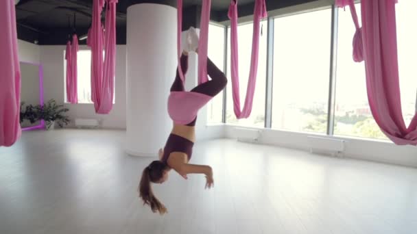 Una giovane ragazza atletica fa yoga su un'amaca, esercizi per la salute. Allenamento in palestra con finestre panoramiche. — Video Stock