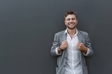 Gülümseyen ve kendine güvenen takım elbiseli bir iş adamının profil portresi. Gri duvarda genç bir adam.