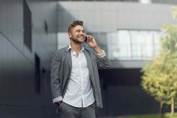 Όμορφος επιχειρηματίας με κουστούμι και μιλάει στο τηλέφωνο στο δρόμο. Πορτρέτο ενός νεαρού άνδρα σε επιχειρηματικό στυλ χαμογελώντας και γελώντας. — Φωτογραφία Αρχείου
