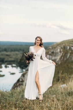 Doğada yürüyen bir buket kurumuş çiçekli gelin. Sonbaharda Boho tarzı düğün.