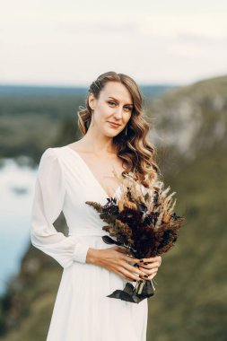 Doğada yürüyen bir buket kurumuş çiçekli gelin. Sonbaharda Boho tarzı düğün.