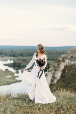 Doğada yürüyen bir buket kurumuş çiçekli gelin. Sonbaharda Boho tarzı düğün.