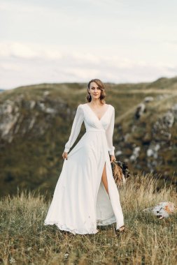 Doğada yürüyen bir buket kurumuş çiçekli gelin. Sonbaharda Boho tarzı düğün.