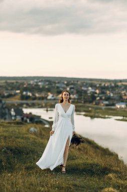 Doğada yürüyen bir buket kurumuş çiçekli gelin. Sonbaharda Boho tarzı düğün.