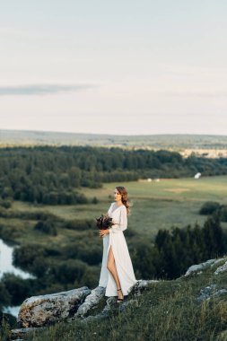 Doğada yürüyen bir buket kurumuş çiçekli gelin. Sonbaharda Boho tarzı düğün.