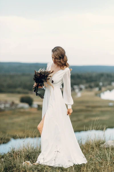 Panna młoda z bukietem suszonych kwiatów spacerujących w przyrodzie. Ślub w stylu Boho jesienią. — Zdjęcie stockowe