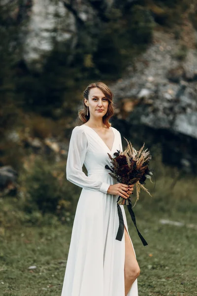 Novia con un ramo de flores secas caminando en la naturaleza. Boda de estilo boho en otoño. —  Fotos de Stock