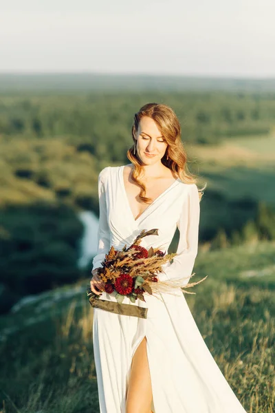 Noiva com um buquê de flores secas andando na natureza. Boho casamento estilo no outono. — Fotografia de Stock