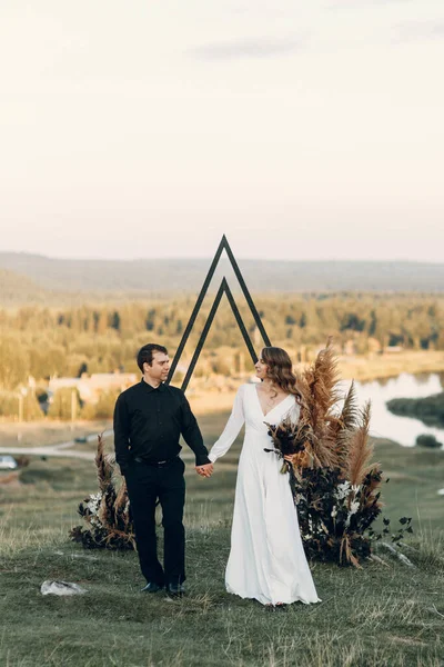 Um noivo elegante beija uma noiva linda à luz do sol, o momento perfeito. Casal de Boho, cerimônia de luxo nas montanhas com vistas deslumbrantes. — Fotografia de Stock