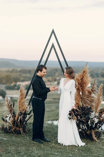 Um noivo elegante beija uma noiva linda à luz do sol, o momento perfeito. Casal de Boho, cerimônia de luxo nas montanhas com vistas deslumbrantes. — Fotografia de Stock