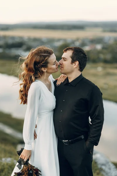 Una hermosa novia feliz de cuento de hadas con un ramo y una corona y un novio con estilo en el fondo de rocas en las montañas. Boda Boho en la naturaleza. — Foto de Stock