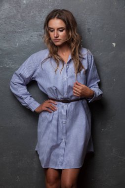 Güzel bir kız uzun erkek gömlek gri duvar tarafından duruyor.