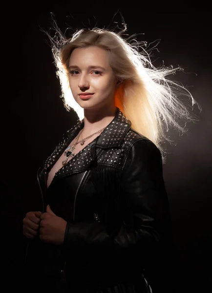 Beautiful blonde girl with flying hair in a black leather jacket on a black background.