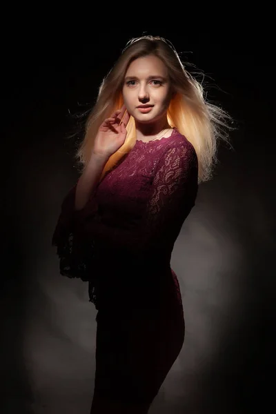 Beautiful blonde girl with flying hair in a red dress on a black background.