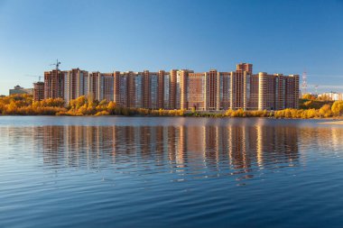 Mavi gökyüzüne karşı yapım aşamasındaki bina gölün yüzeyine yansıyor..