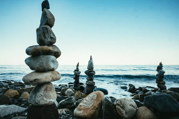 Zen style balanced stones on beach. Rock sculpture stone stacking. A stone pyramid on sea shore. Stones balance on a background of sea and blue sky.
