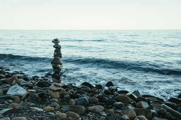 Zen style balanced stones on beach. Rock sculpture stone stacking. A stone pyramid on sea shore. Stones balance on a background of sea and blue sky.