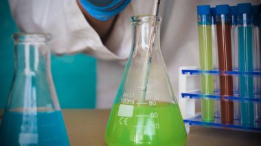 Simyacı, şişeler tutan, bir testin farklı kompozisyonlar, beyaz önlük, solunum, Gözlük, beyaz eldivenleri, yeşil bir arka plan ile test tüpleri testleri.