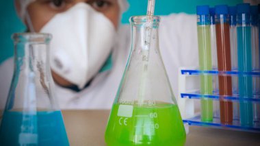Simyacı, şişeler tutan, bir testin farklı kompozisyonlar, beyaz önlük, solunum, Gözlük, beyaz eldivenleri, yeşil bir arka plan ile test tüpleri testleri.