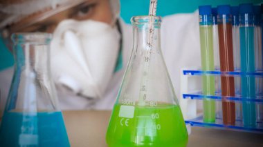 Simyacı, şişeler tutan, bir testin farklı kompozisyonlar, beyaz önlük, solunum, Gözlük, beyaz eldivenleri, yeşil bir arka plan ile test tüpleri testleri.