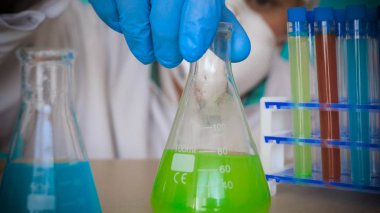 Simyacı, şişeler tutan, bir testin farklı kompozisyonlar, beyaz önlük, solunum, Gözlük, beyaz eldivenleri, yeşil bir arka plan ile test tüpleri testleri.