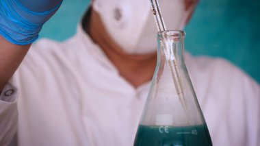 Simyaci bir biyolog, solunum, Gözlük, beyaz bir tıbbi elbisesi, bir şişesi, yeşil bir arka plan, bir bilim tablo içinde bir koruyucu kapak içinde çeşitli maddeler, Dna alır.