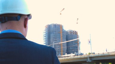 Oluşturucu veya mühendis, duruyor onun binaları, seyir sırt ile beyaz bir miğfer ve Evet, bir gökdelen bir takım elbise