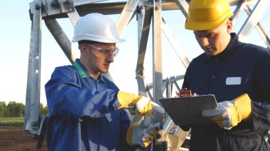 Bir elektrikçi veya Oluşturucusu ve mühendis, sarı ve beyaz kask içinde mavi bir elbise içinde güç için teknik genel bakış kontrol, elektrik direkleri, bir elektrik Kulesi, enerji ve işçi hazırlamak.