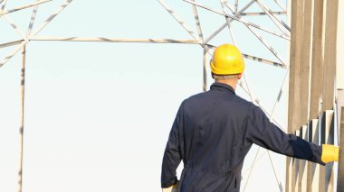 Bir elektrikçi veya sarı miğfer Oluşturucu, bir çalışan mavi bir elbise içinde elektrik direkleri, bir elektrik Kulesi ve enerji yüklemeye hazırlanıyor.
