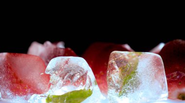 Dondurulmuş çilek ve nane yaprakları buz küpleri, duman, siyah arka plan.