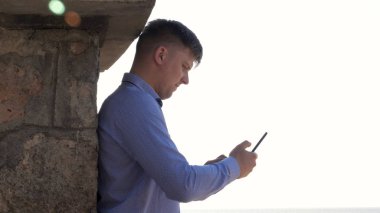 Yakışıklı adam (erkek) bir duvara karşı duran genç bir cep telefonu, denizde bir ileti yazar. Konsept: iletişim, internet, ağ.