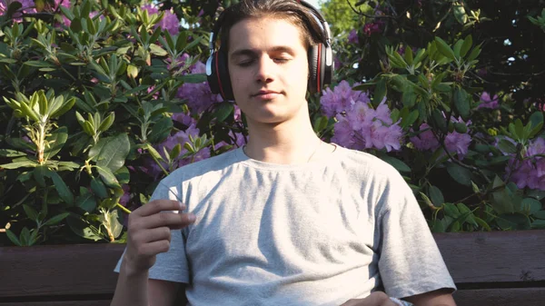 Genç Yakışıklı Adam Genç Parkta Bir Bankta Oturur Müziği Dinliyor — Stok fotoğraf
