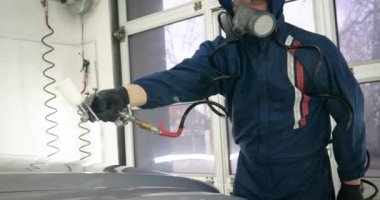 Ağır çekimde, elinde sprey tabanca ve koruyucu gözlüklü bir solunum cihazıyla çalışan bir erkek (erkek), elinde klasörlü bir el feneri ile bir araba motorunu kontrol eder. Otomatik merkez kavramı.