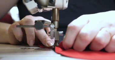 Malzeme her iki tarafını kullanarak kırmızı kumaş üzerinde profesyonel bir makine, nakış (sews) ile terzi dikiş elleri. Konsept: fabrika, ev, Iş başında, profesyoneller.