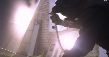 Yavaş hareket profesyonel bir adam (adam) bir garaj (hizmet) bir kazak giymiş çalışma giysileri içinde bir boya tabancası (püskürtme tabancası) ayarlar ve (seramik bir tabaka koyarak) bir yat boyama başlar.