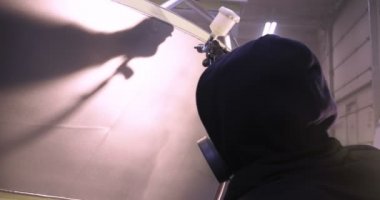 Yavaş hareket profesyonel bir adam (adam) bir garaj (hizmet) bir kazak giymiş çalışma giysileri içinde bir boya tabancası (püskürtme tabancası) ayarlar ve (seramik bir tabaka koyarak) bir yat boyama başlar.