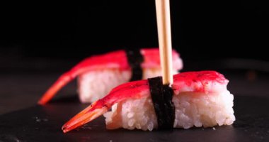 Bir tepsi üzerinde koyu bir arka plan üzerinde, pişmiş veya satın suşi (Nigiri) Çin yemek çubukları tadı. Konsept: Nigiri, Günün Suşi, İki, Lezzetli, Çubuklar, Çok Yakın, Yavaş Hareket.