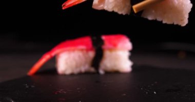 Bir tepsi üzerinde koyu bir arka plan üzerinde, pişmiş veya satın suşi (Nigiri) Çin yemek çubukları tadı. Konsept: Nigiri, Günün Suşi, İki, Lezzetli, Çubuklar, Çok Yakın, Yavaş Hareket.