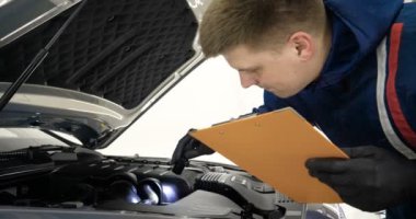 Ağır çekimde, elinde sprey tabanca ve koruyucu gözlüklü bir solunum cihazıyla çalışan bir erkek (erkek), elinde klasörlü bir el feneri ile bir araba motorunu kontrol eder. Otomatik merkez kavramı.