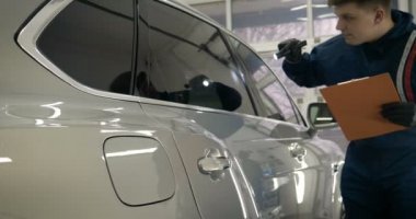 Ağır çekimde, elinde sprey tabanca ve koruyucu gözlüklü bir solunum cihazıyla çalışan bir erkek (erkek), elinde klasörlü bir el feneri ile bir araba motorunu kontrol eder. Otomatik merkez kavramı.